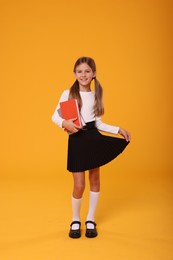 Photo of Happy schoolgirl with books on orange background