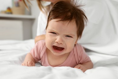 Photo of Crying little baby lying on white bed