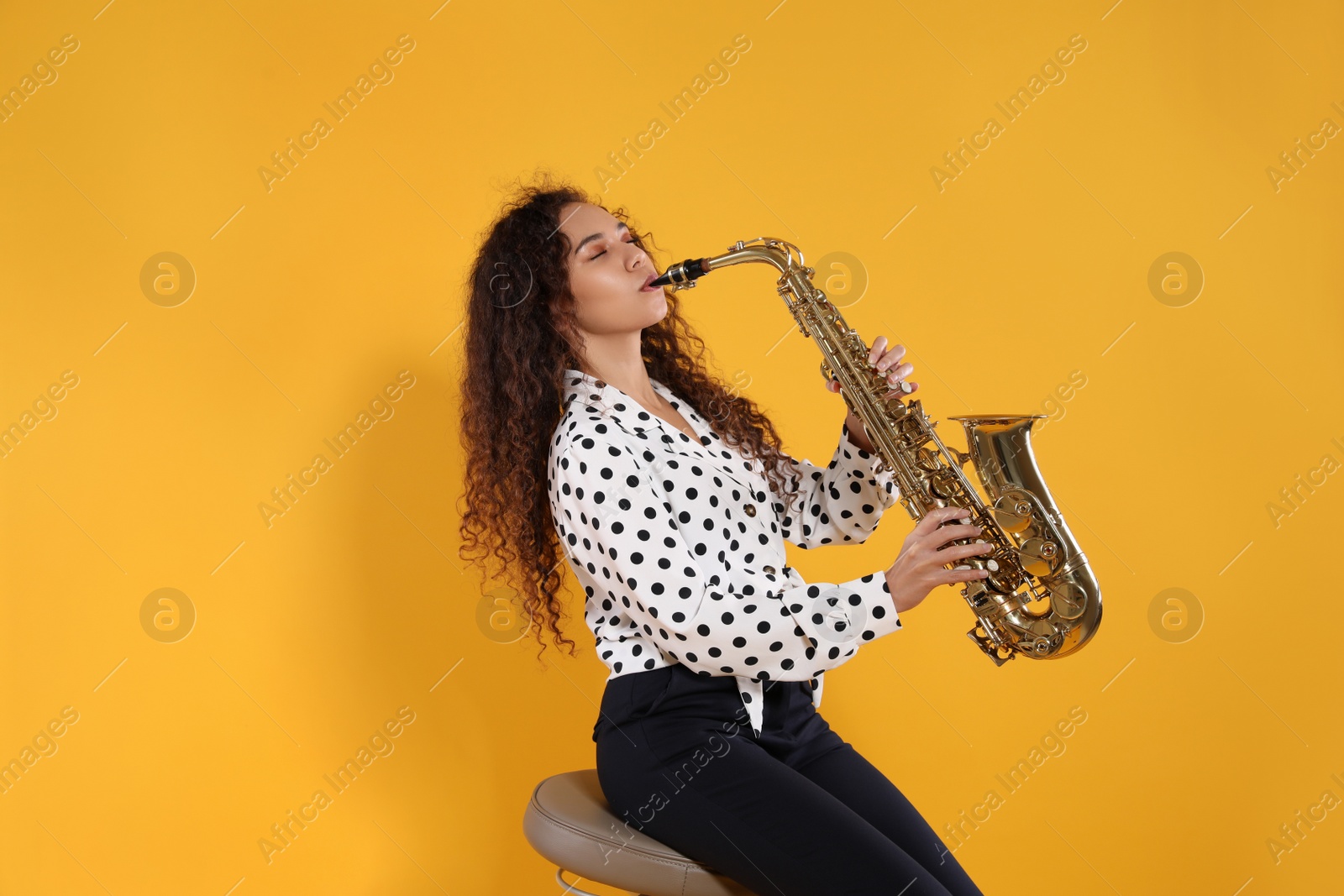 Photo of Beautiful African American woman playing saxophone on yellow background