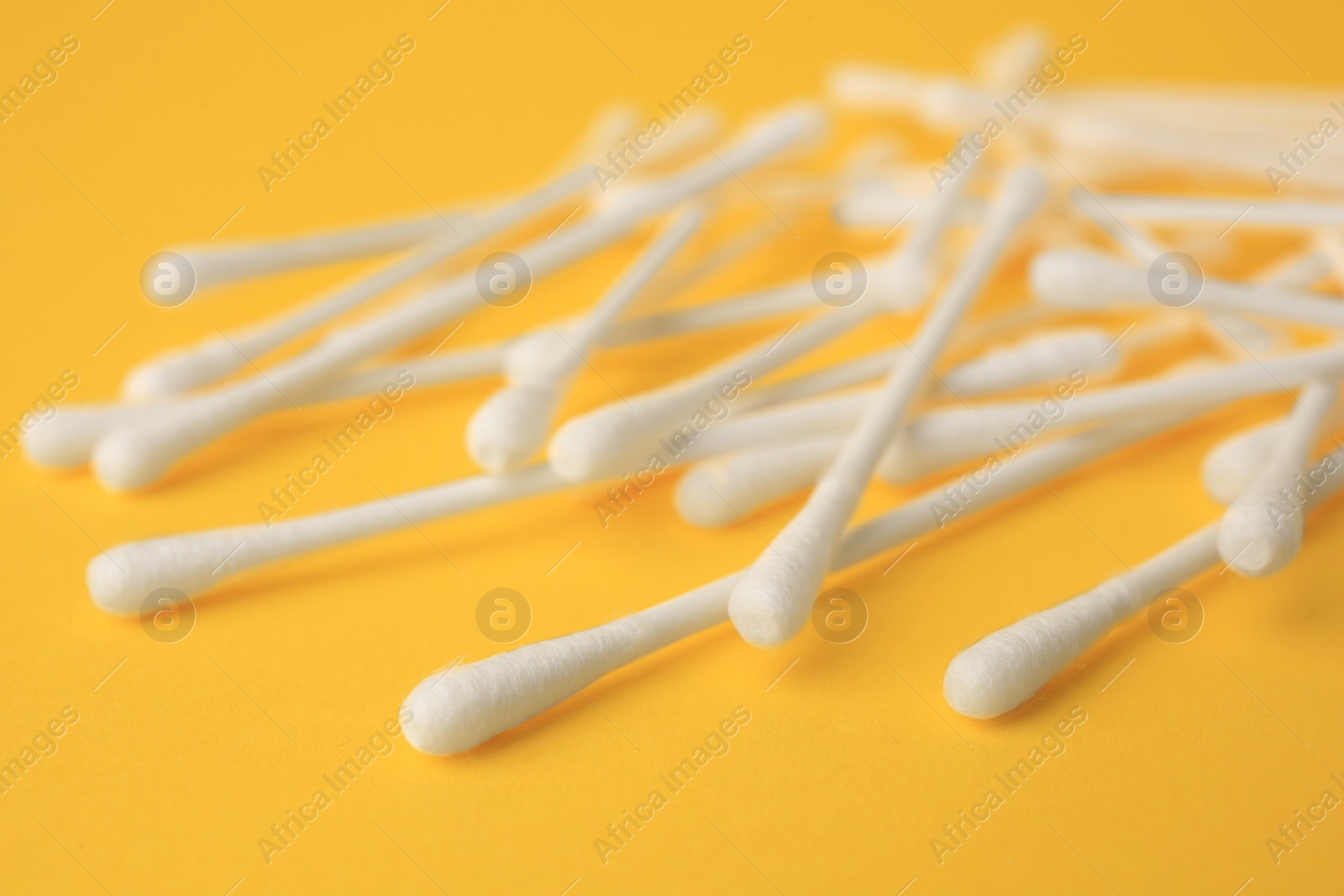 Photo of Many clean cotton buds on yellow background, closeup