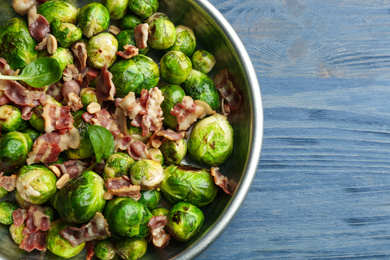 Photo of Delicious Brussels sprouts with bacon on blue wooden table, top view