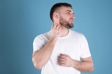 Man scratching neck on color background. Allergy symptoms