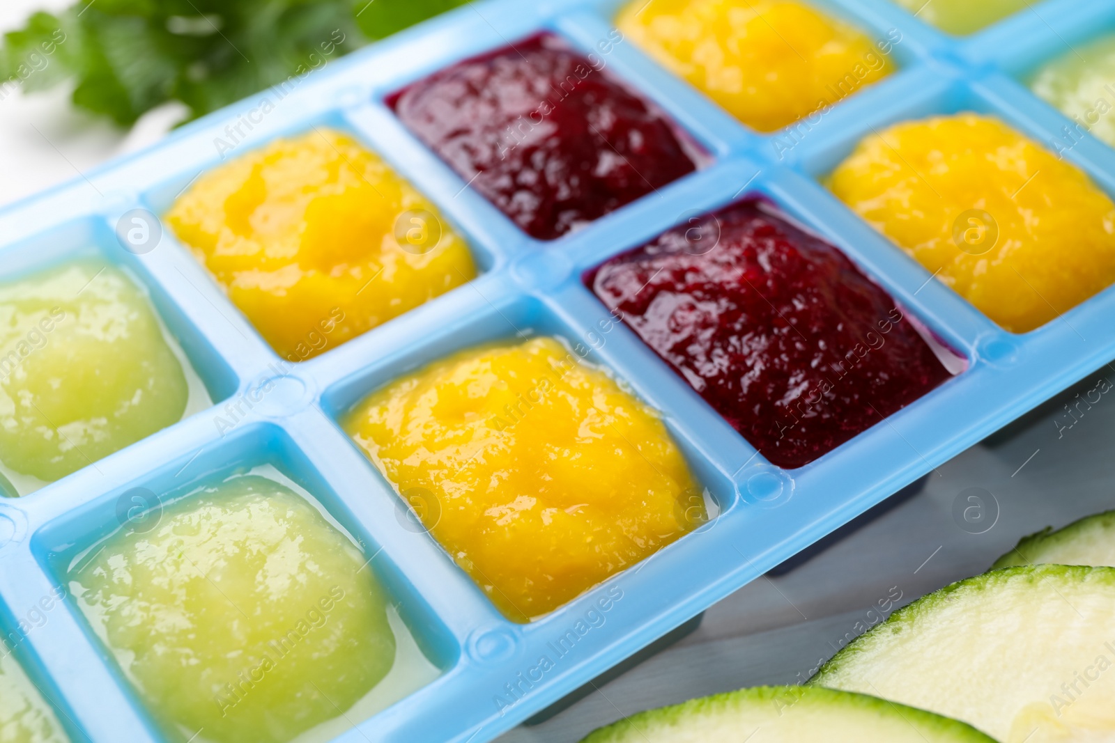 Photo of Different purees in ice cube tray and ingredients on table, closeup. Ready for freezing