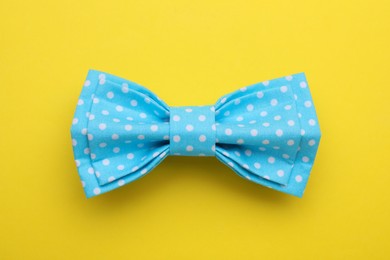 Stylish light blue bow tie with polka dot pattern on yellow background, top view