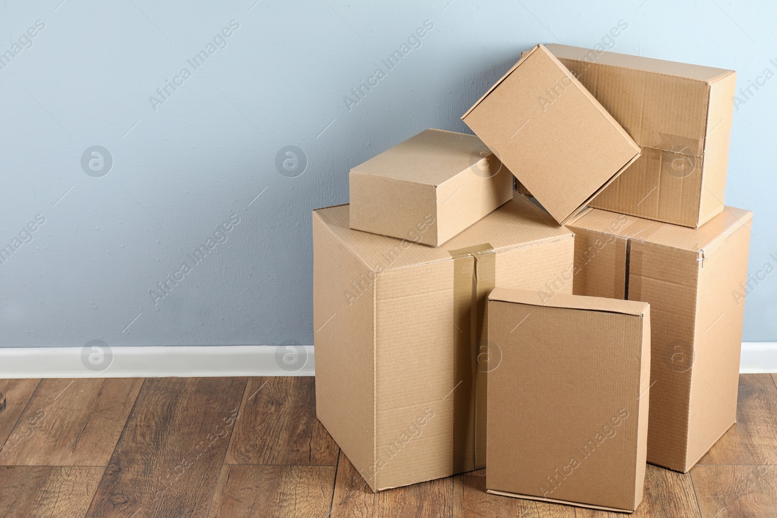 Photo of Pile of cardboard boxes near light blue wall indoors. Space for text