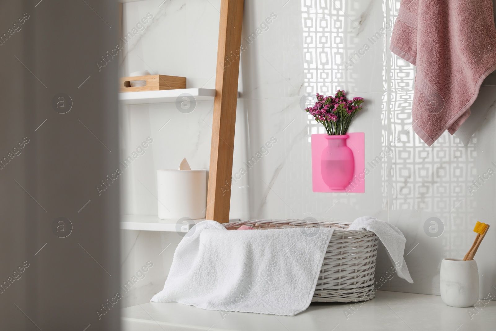 Photo of Silicone vase with flowers on white marble wall over countertop in stylish bathroom