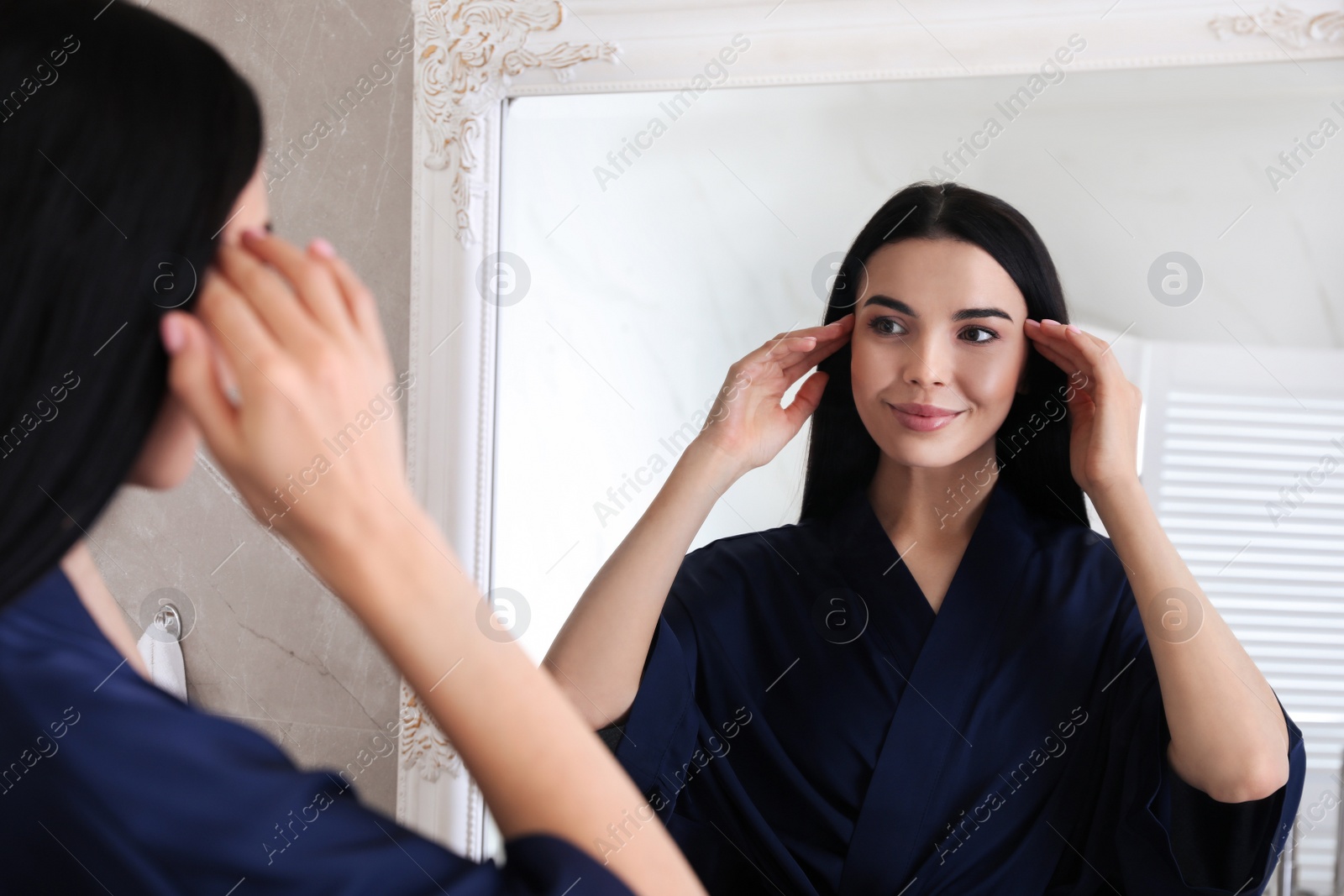 Photo of Beautiful young woman looking at herself in bathroom mirror