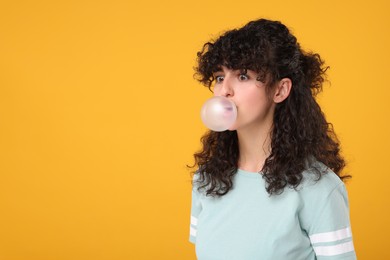 Beautiful young woman blowing bubble gum on orange background. Space for text