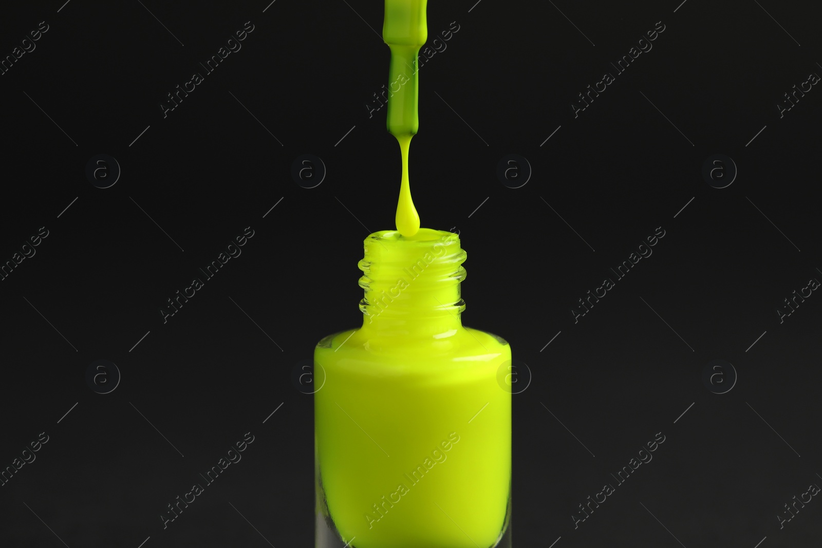 Photo of Neon green nail polish dripping from brush into bottle on black background, closeup