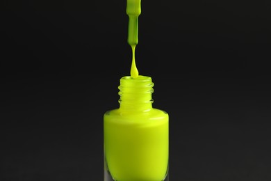 Neon green nail polish dripping from brush into bottle on black background, closeup