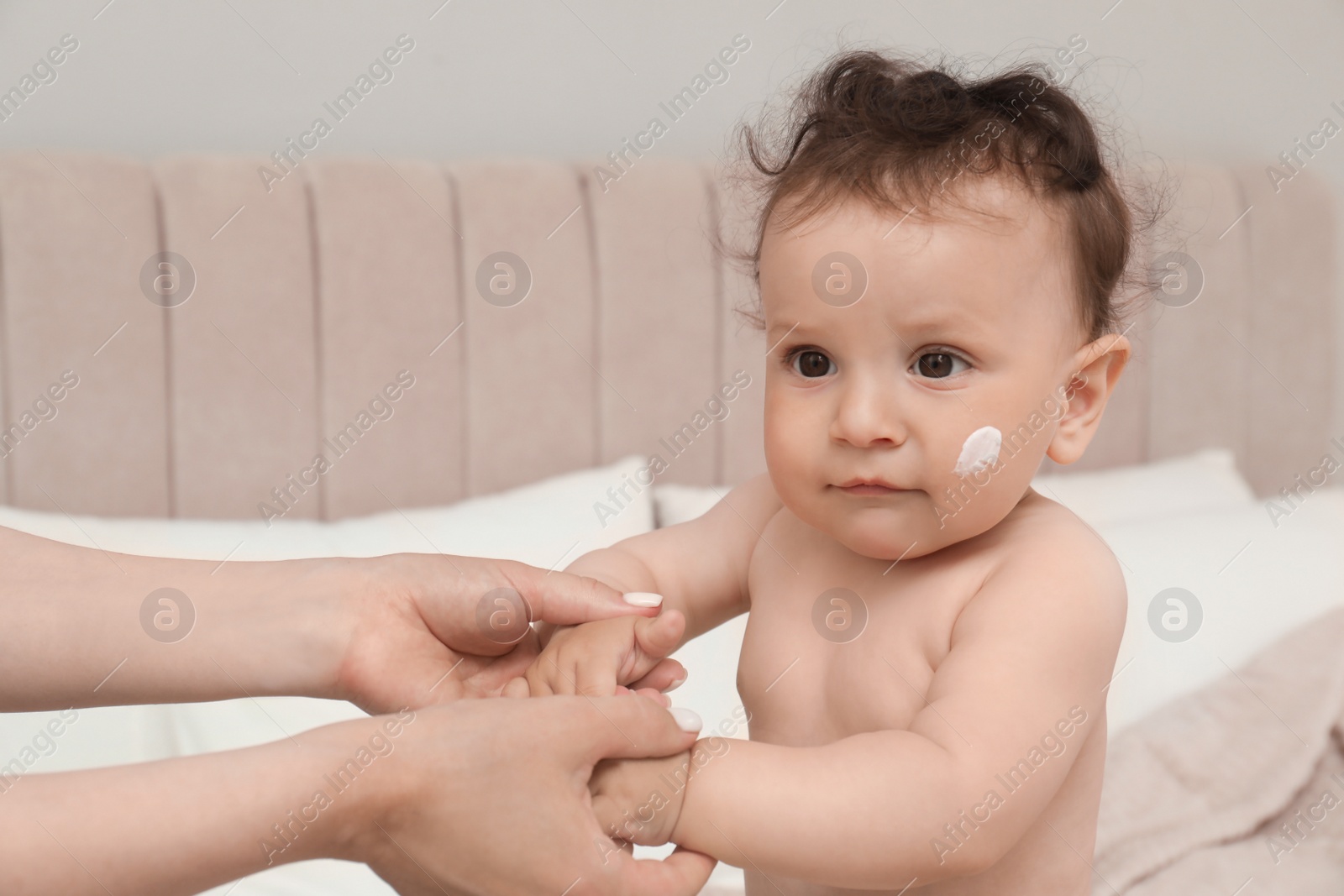 Photo of Mother applying body cream on her baby in bedroom