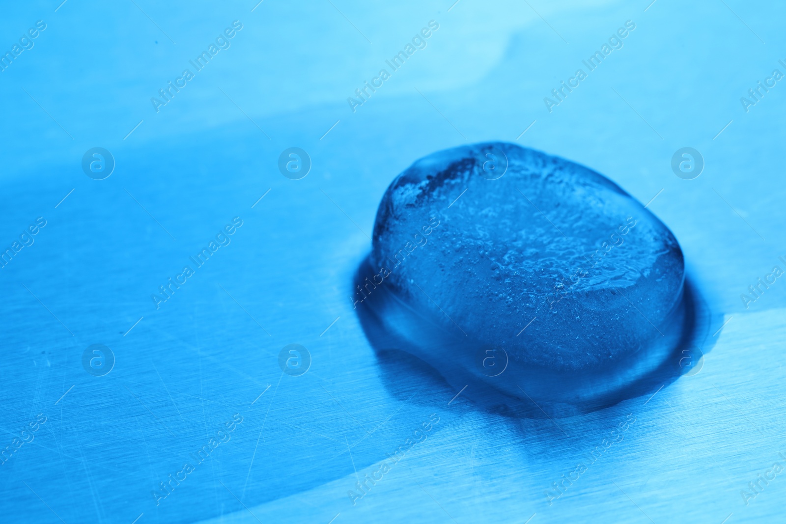 Photo of Crystal clear ice cube on light blue background, space for text. Color tone effect