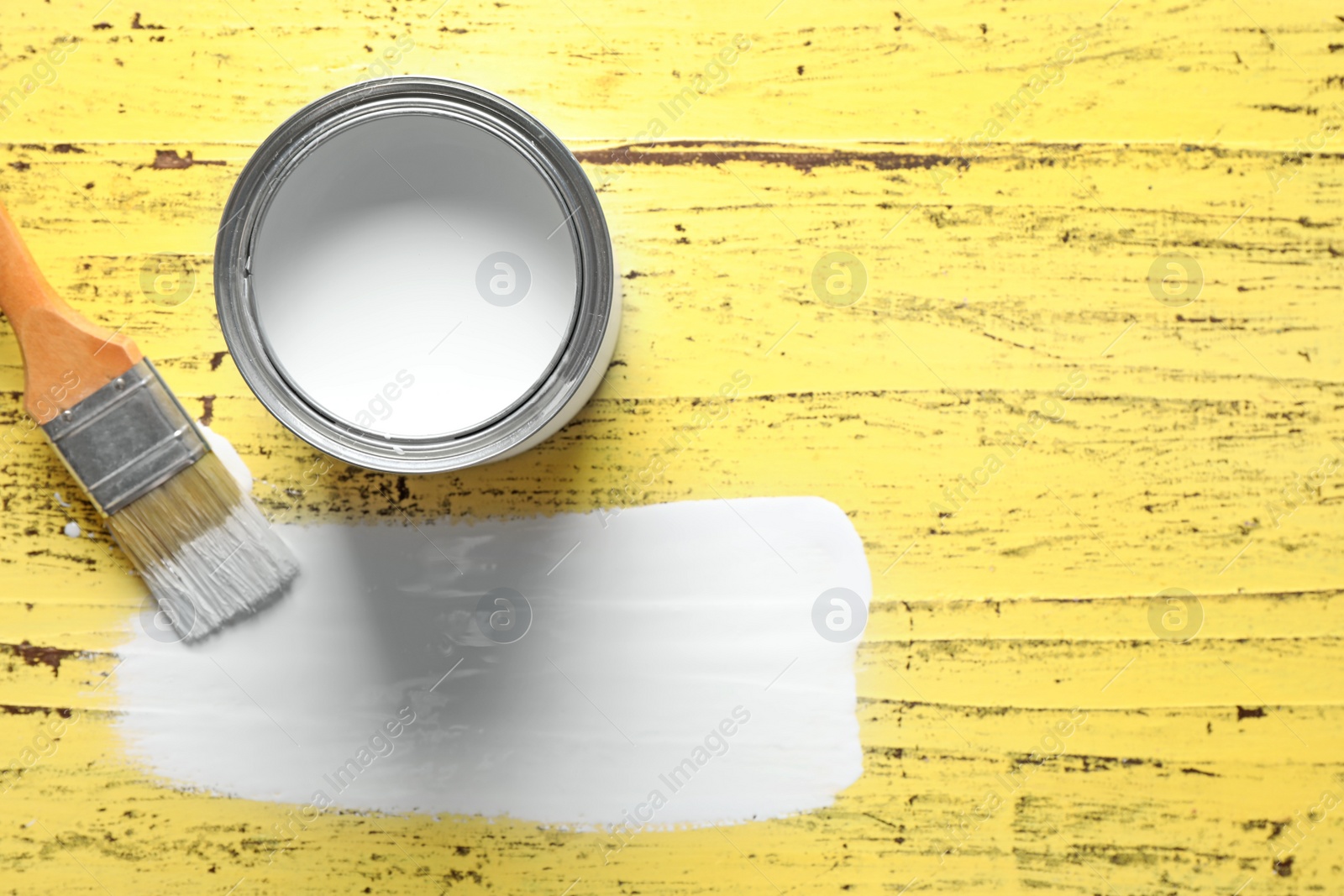 Photo of Open can, brush and paint stroke on yellow wooden table, flat lay. Space for text