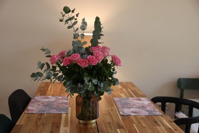 Beautiful bouquet of roses and eucalyptus branches in vase near napkins on wooden table indoors