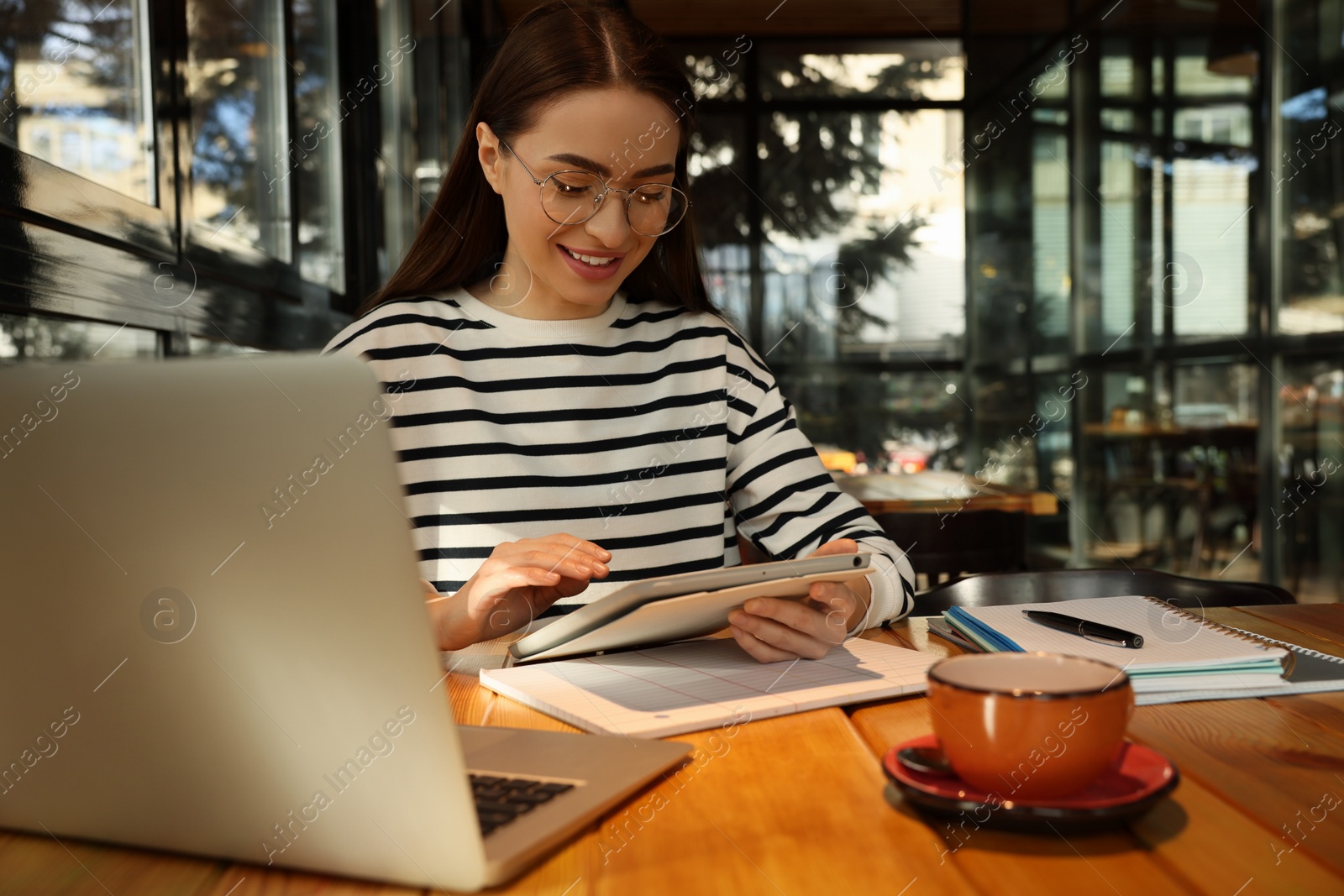 Photo of Young female student with laptop and tablet studying at table in cafe