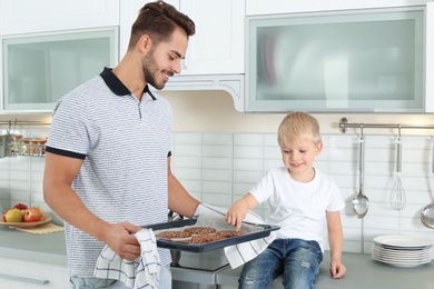 Young man treating his son with homemade oven baked cookies in kitchen