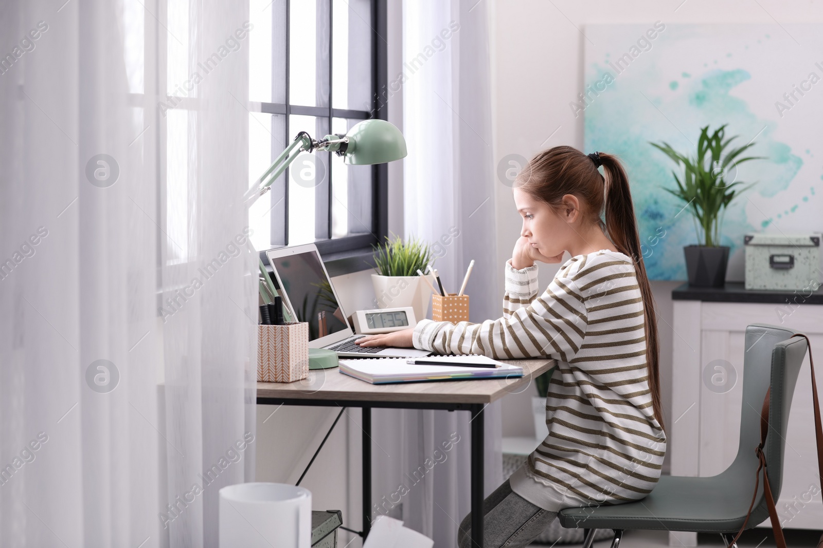 Photo of Pretty preteen girl doing homework at table in room