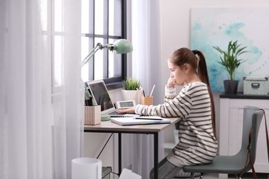 Pretty preteen girl doing homework at table in room