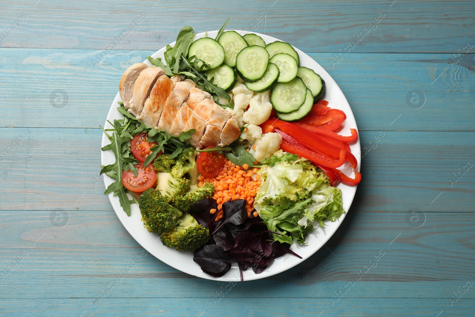 Photo of Balanced diet and healthy foods. Plate with different delicious products on light blue wooden table, top view