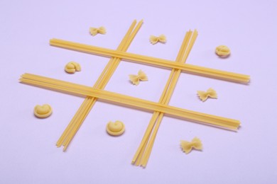 Tic tac toe game made with different types of pasta on lilac background