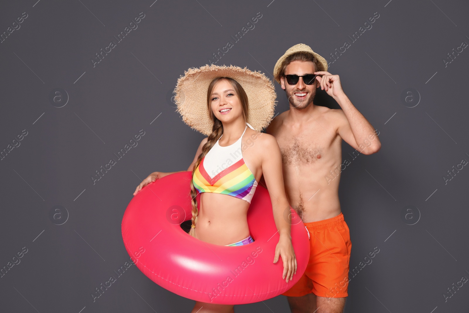 Photo of Young couple in beachwear with inflatable ring on dark background