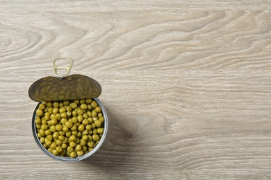 Open tin can of peas on wooden background, top view. Space for text