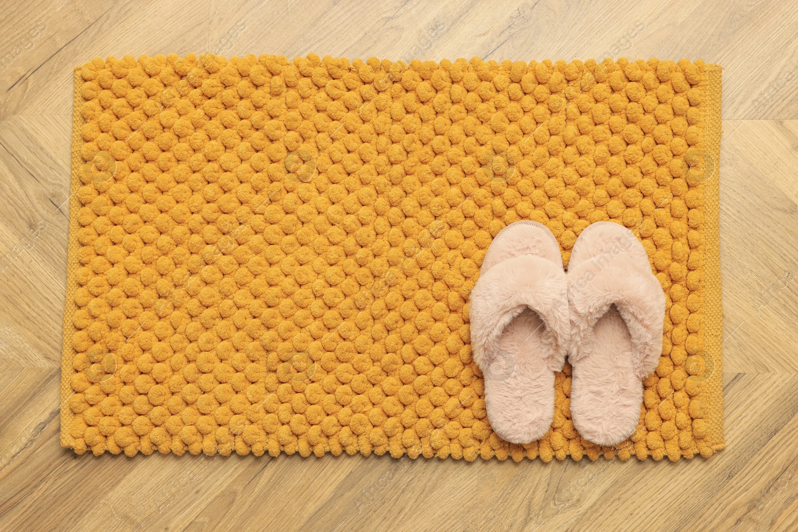 Photo of Soft orange bath mat and slippers on floor, top view