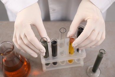 Woman taking test tubes with different types of crude oil from rack at grey table, closeup