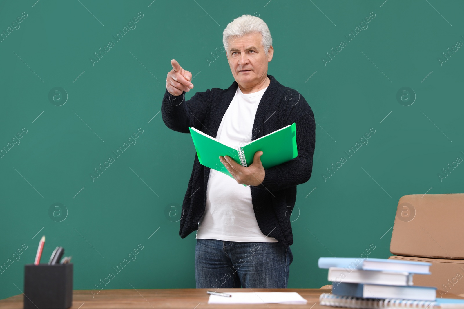 Photo of Portrait of senior teacher with notebook at green chalkboard and table