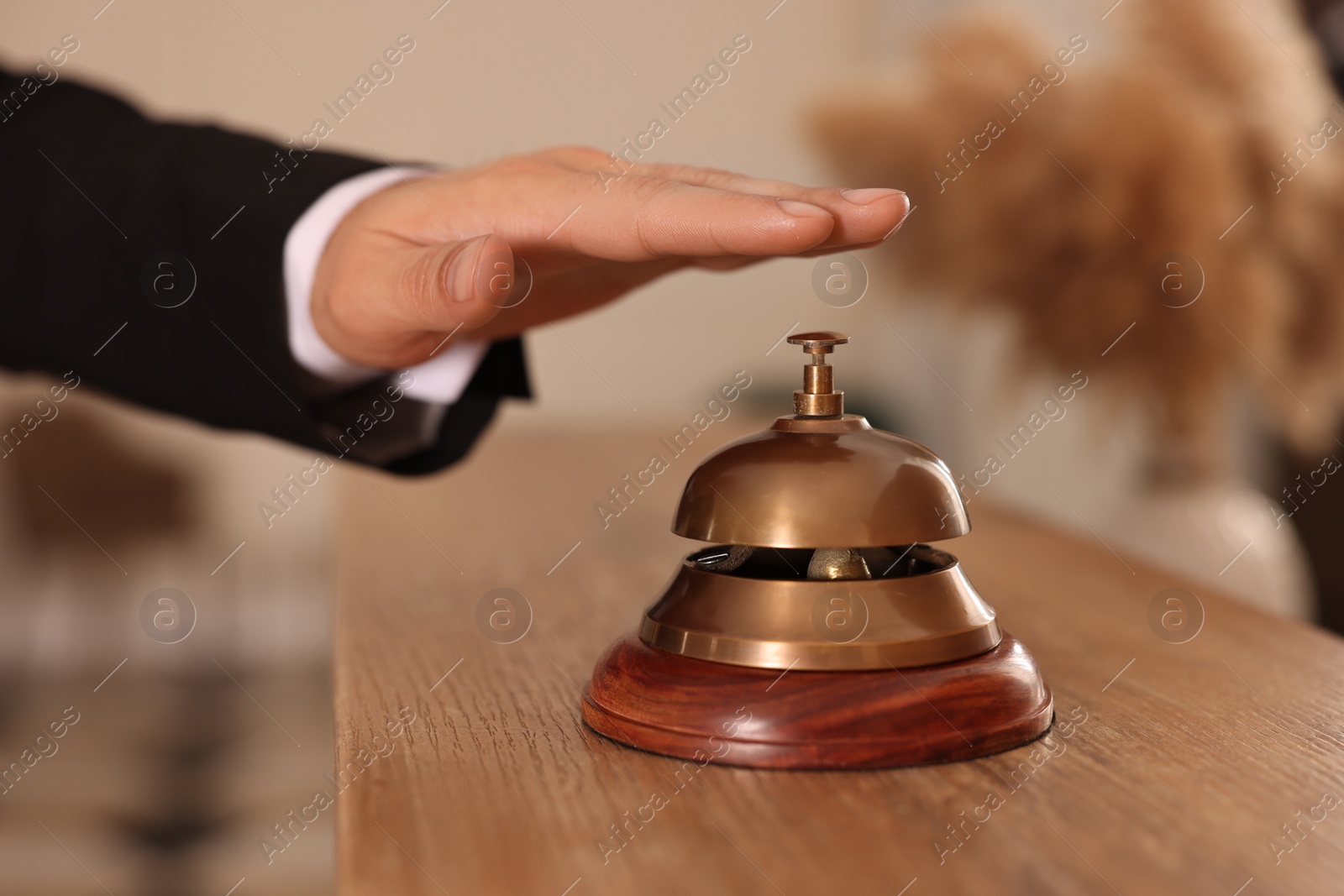 Photo of Man ringing service bell at wooden reception desk in hotel, closeup