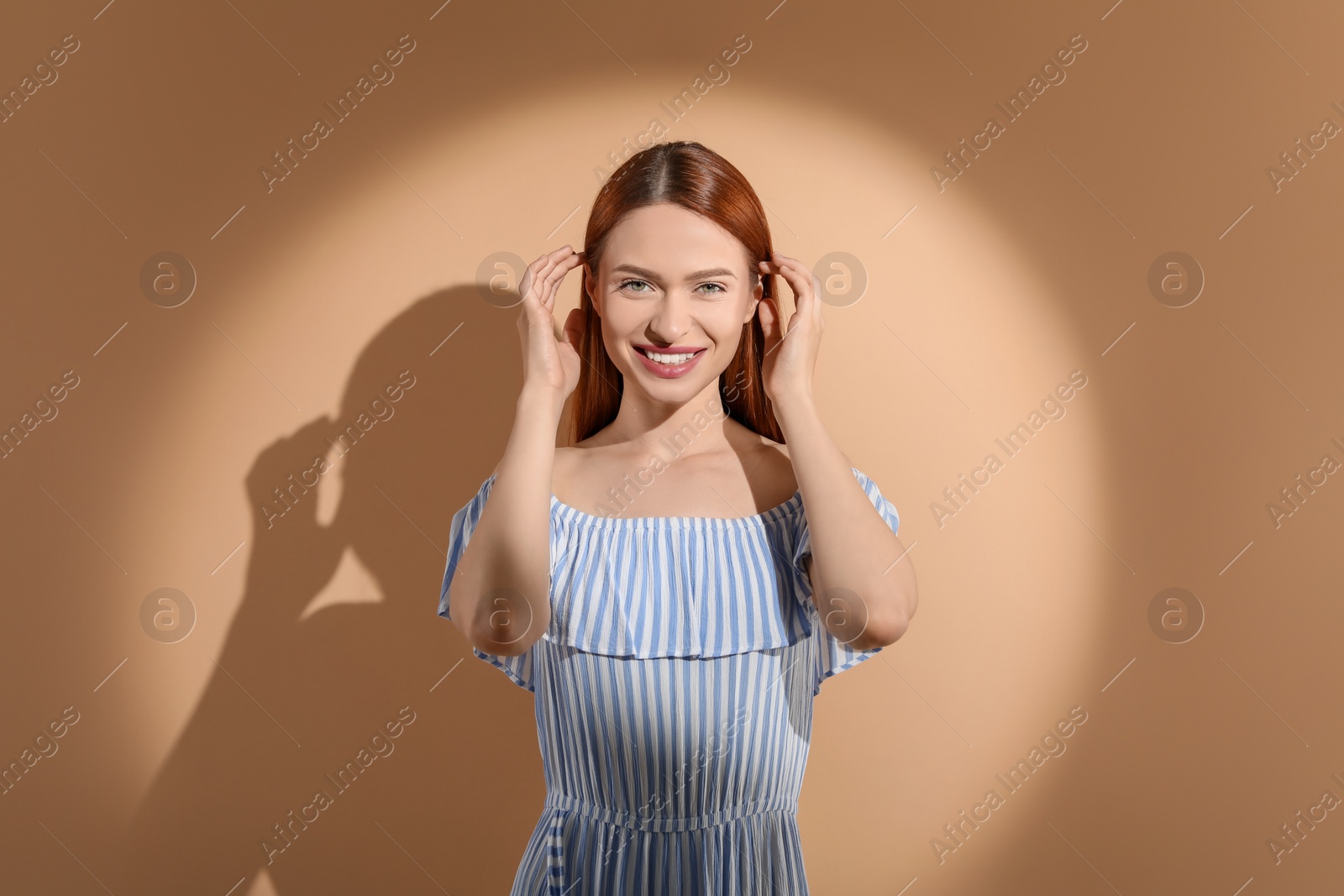 Photo of Beautiful young woman in sunlight on beige background