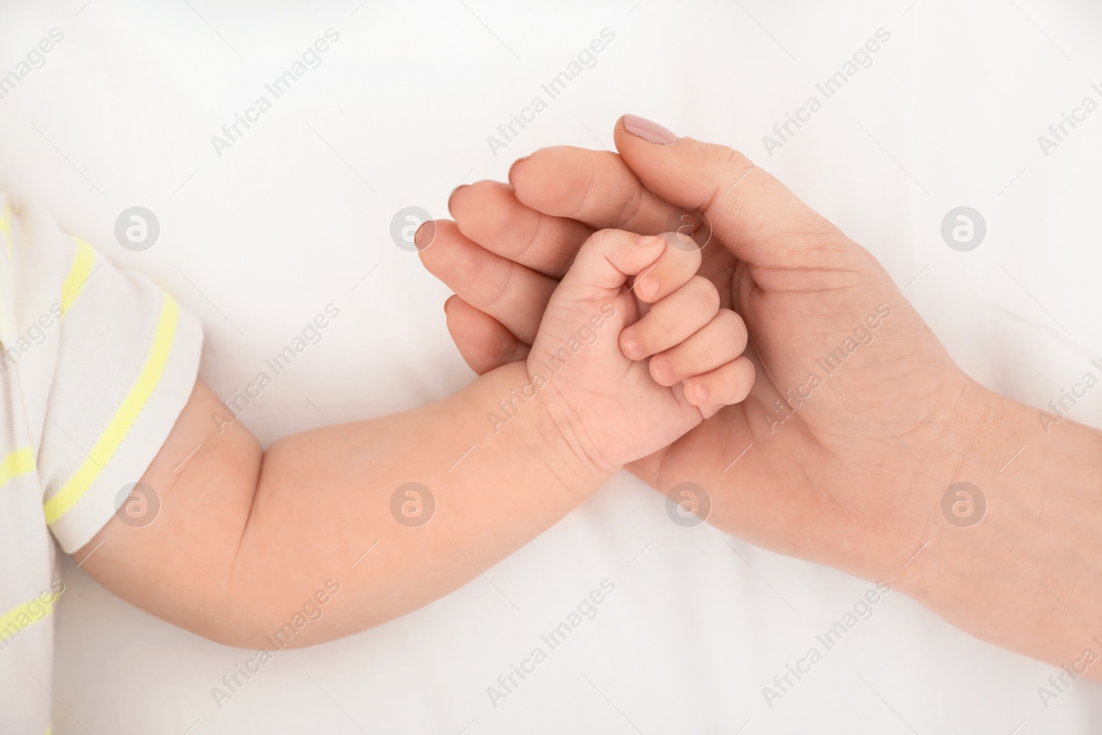 Photo of Mother holding baby's hand on bed, top view
