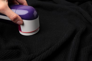 Woman using fabric shaver on black cloth with lint, closeup. Space for text