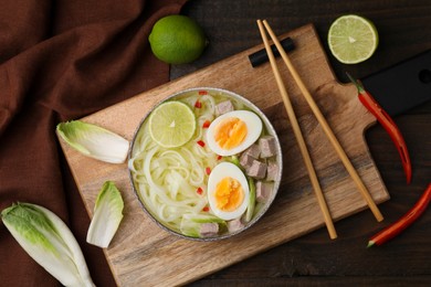 Photo of Bowl of delicious rice noodle soup with meat and egg on wooden table, flat lay