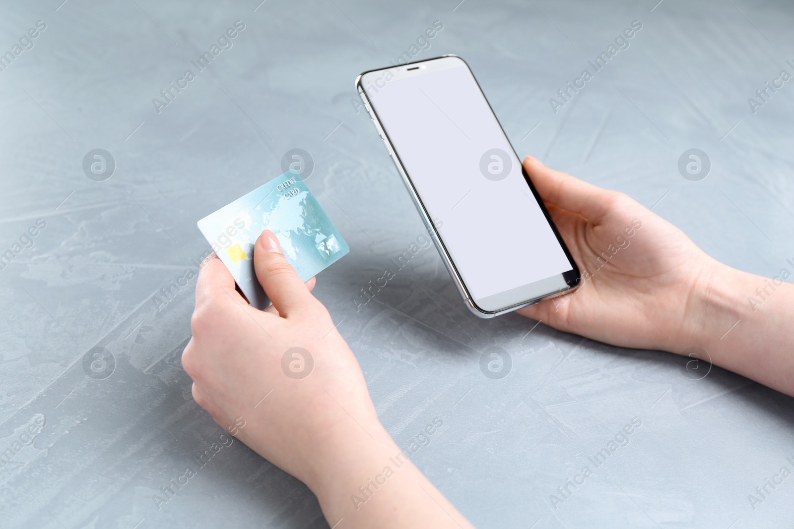 Photo of Online payment. Woman with smartphone and credit card at white table, closeup