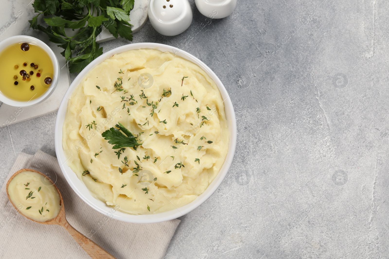 Photo of Bowl of tasty mashed potato, parsley, olive oil and pepper on grey marble table, flat lay. Space for text