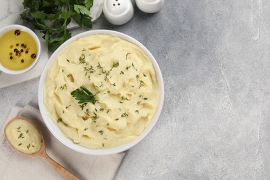 Bowl of tasty mashed potato, parsley, olive oil and pepper on grey marble table, flat lay. Space for text