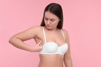 Photo of Mammology. Woman in bra doing breast self-examination on pink background