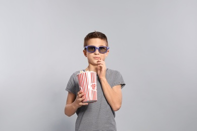 Boy with 3D glasses and popcorn during cinema show on grey background