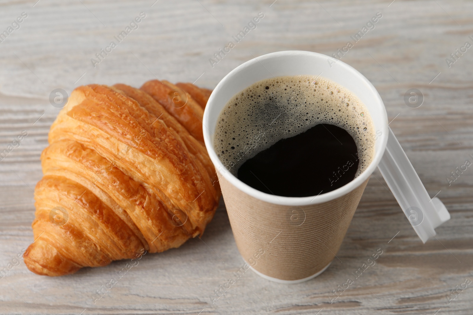 Photo of Coffee to go. Paper cup with tasty drink and croissant on white wooden table, closeup