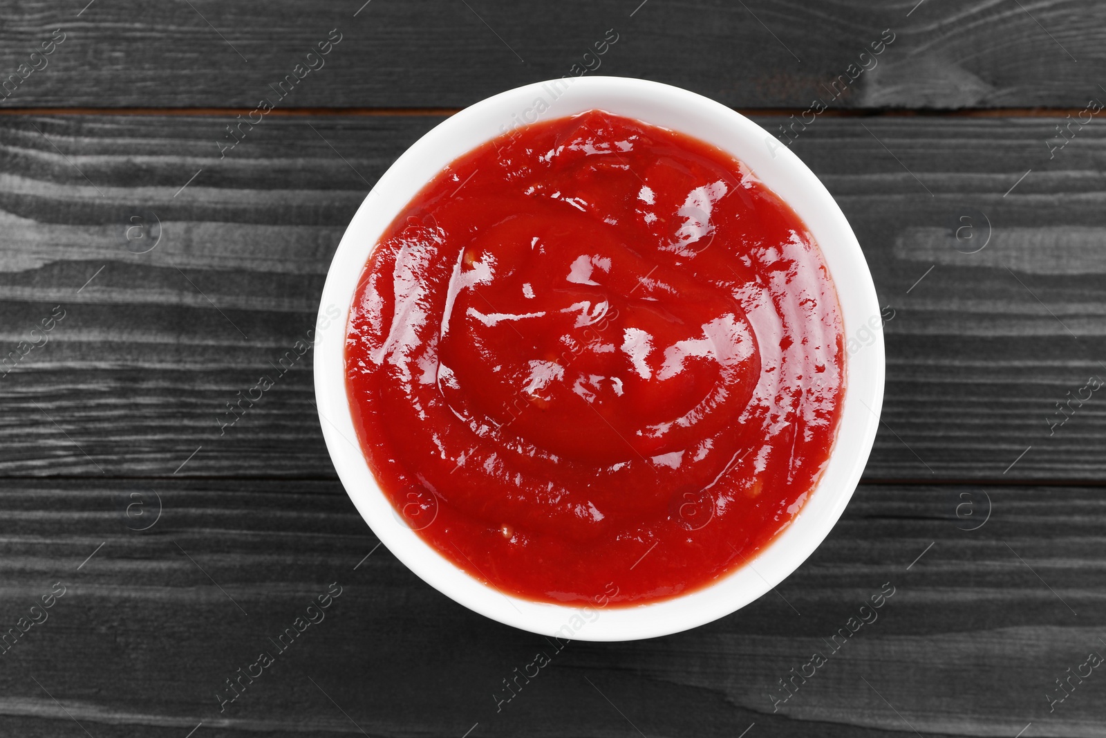 Photo of Delicious ketchup in bowl on black wooden table, top view. Tomato sauce