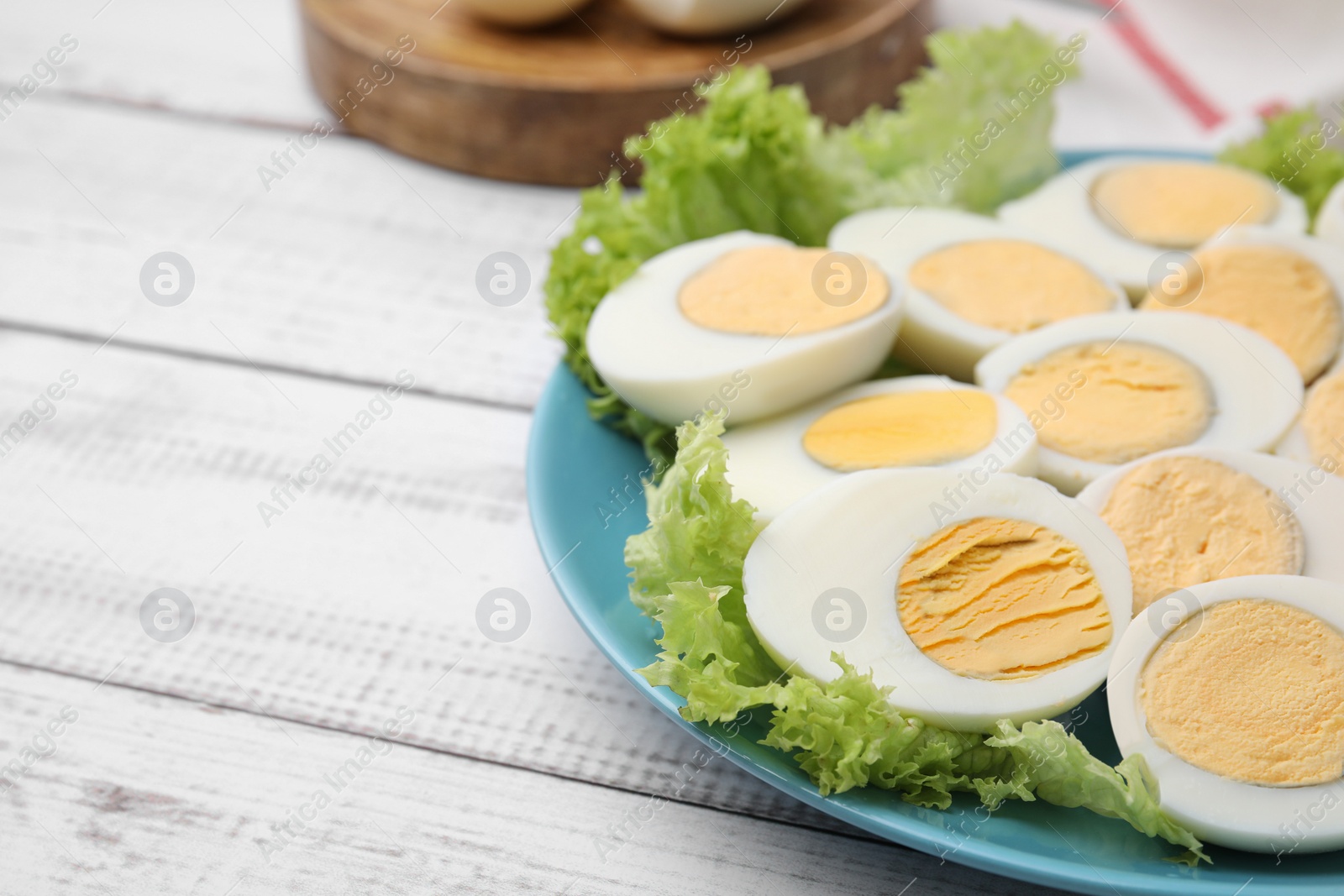 Photo of Fresh hard boiled eggs and lettuce on white wooden table. Space for text