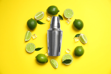 Photo of Flat lay composition with fresh juicy limes, ice cubes and cocktail shaker on yellow background