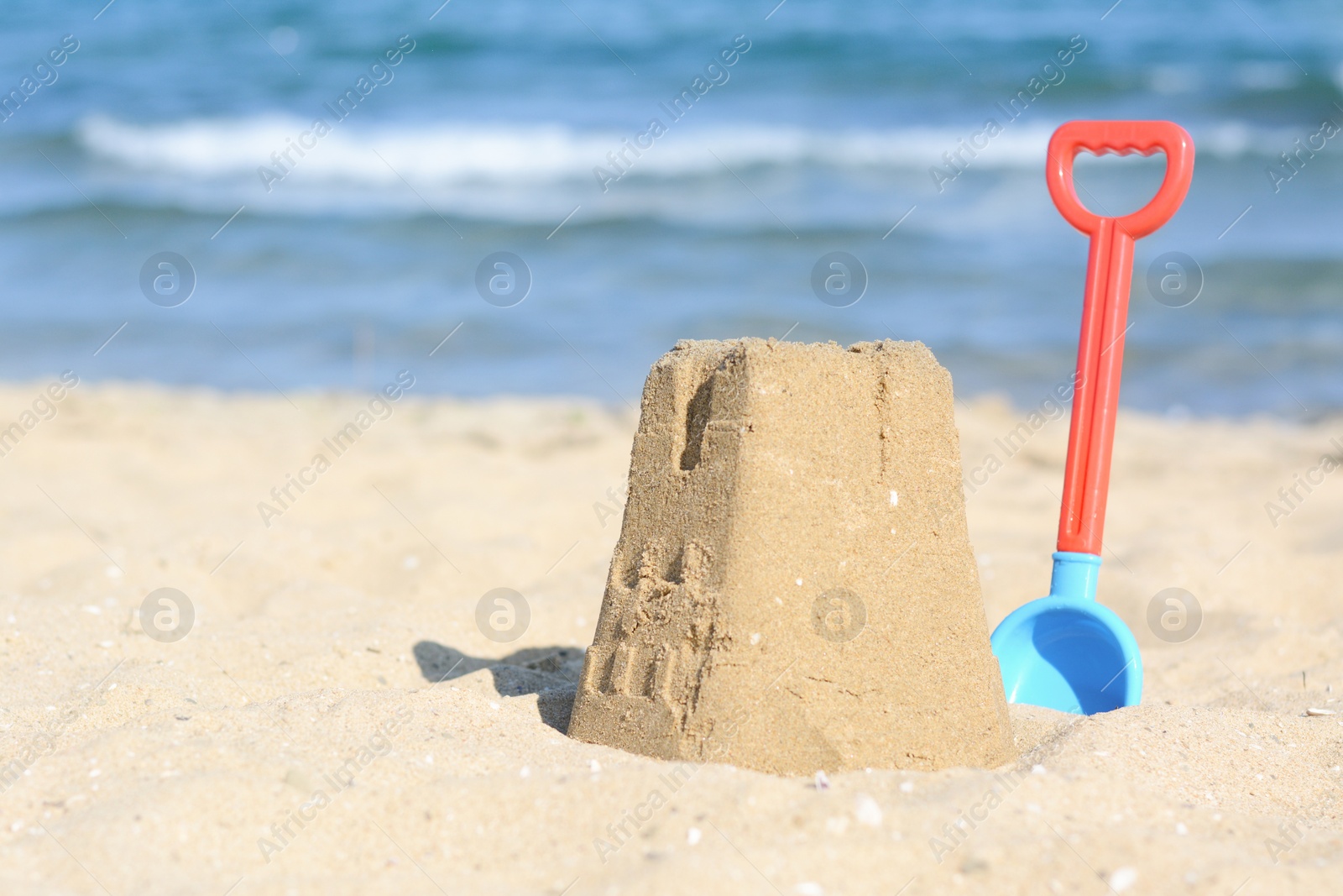 Photo of Beautiful sand castle and plastic shovel on beach near sea, space for text