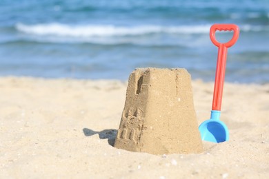 Photo of Beautiful sand castle and plastic shovel on beach near sea, space for text