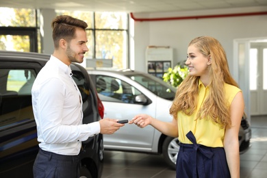 Young salesman giving car key to client in dealership