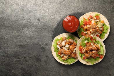 Delicious tacos with vegetables, meat and ketchup on grey textured table, top view. Space for text