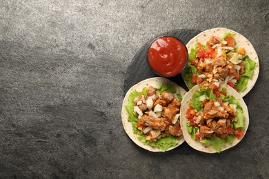 Photo of Delicious tacos with vegetables, meat and ketchup on grey textured table, top view. Space for text