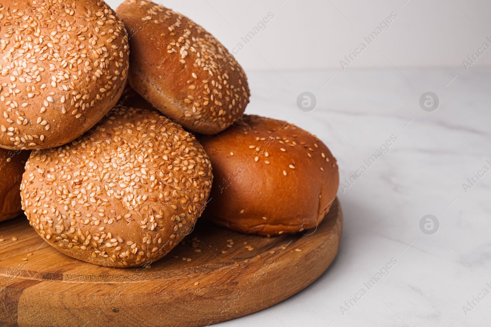 Photo of Fresh buns with sesame seeds on white marble table. Space for text