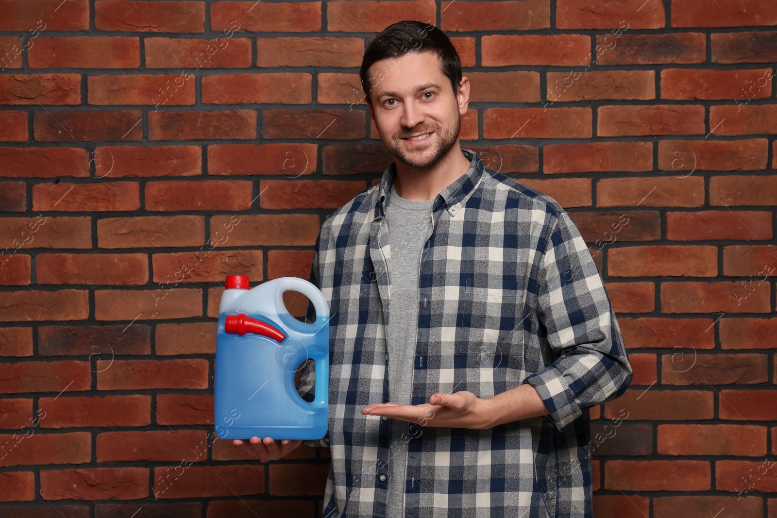 Photo of Handsome man showing canister with blue liquid near brick wall